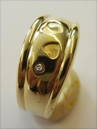 Goldring 18 mm besetzt mit einem strahlenden Diamanten 8/8 W/P, eingearbeitet in feinem Gelbgold 333-, mit 2 Herzmotiven. Maße: Breite 8, Staerke 2,14, Gewicht 2,2, Ringgroesse 18, poliert. Ein elegantes Unikat in feinster Goldschmiedehandarbeit gefertigt